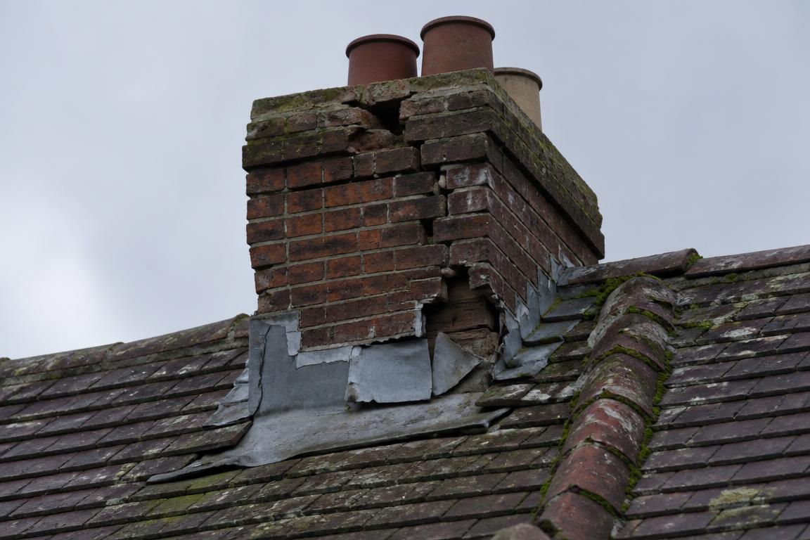Cracked crumbling chimney stack with failed lead flashing and loose ridge tiles